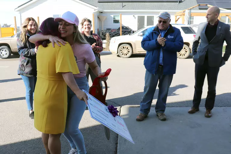 Woman in a pink hat hugging a woman in yellow dress holding a giant check