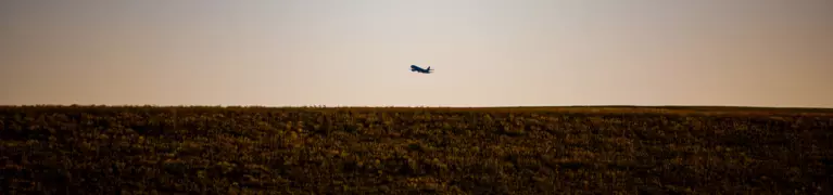 Image of a plane flying over a field at sunset
